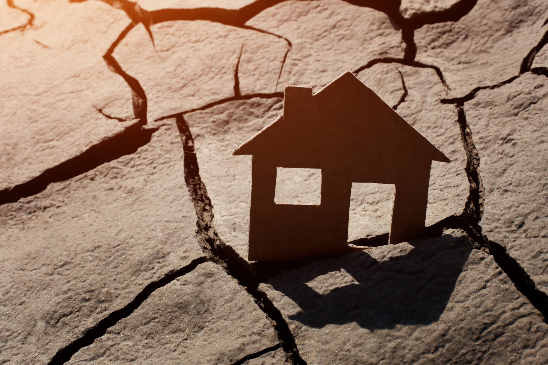 forme en carton d'une façade de maison posée sur un sol craquelé victime de sécheresse